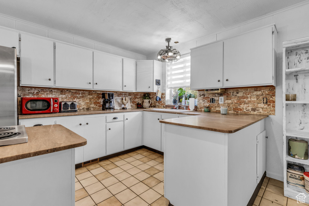 Kitchen featuring appliances with stainless steel finishes, kitchen peninsula, backsplash, light tile patterned floors, and decorative light fixtures