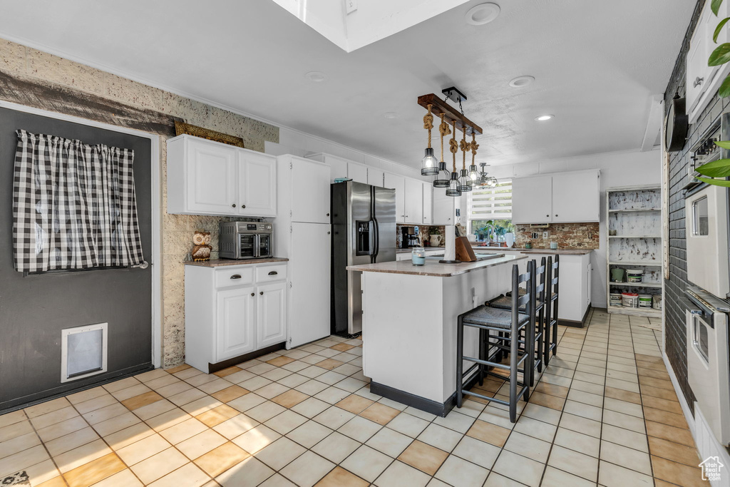 Kitchen with a center island, white cabinetry, tasteful backsplash, and decorative light fixtures