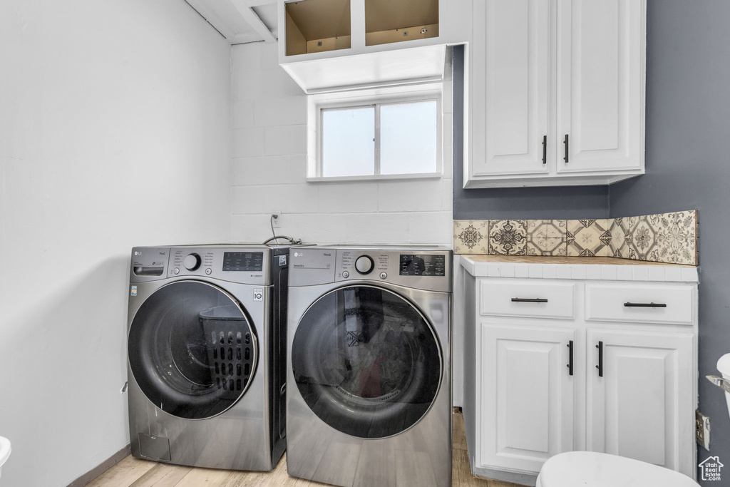 Clothes washing area featuring separate washer and dryer, light hardwood / wood-style flooring, and cabinets