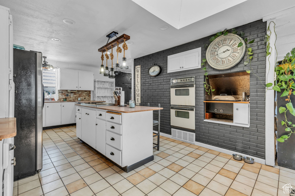 Kitchen featuring white double oven, white cabinetry, pendant lighting, black fridge, and light tile patterned floors