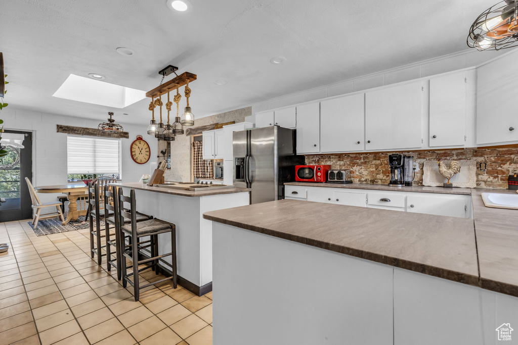 Kitchen with a skylight, light tile patterned floors, a center island, hanging light fixtures, and stainless steel fridge