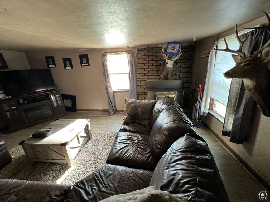 Living room featuring a textured ceiling, wood finished floors, baseboards, and a brick fireplace