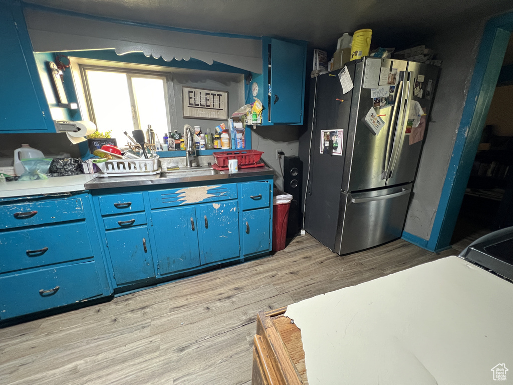 Kitchen with light wood-type flooring, blue cabinets, freestanding refrigerator, and a sink
