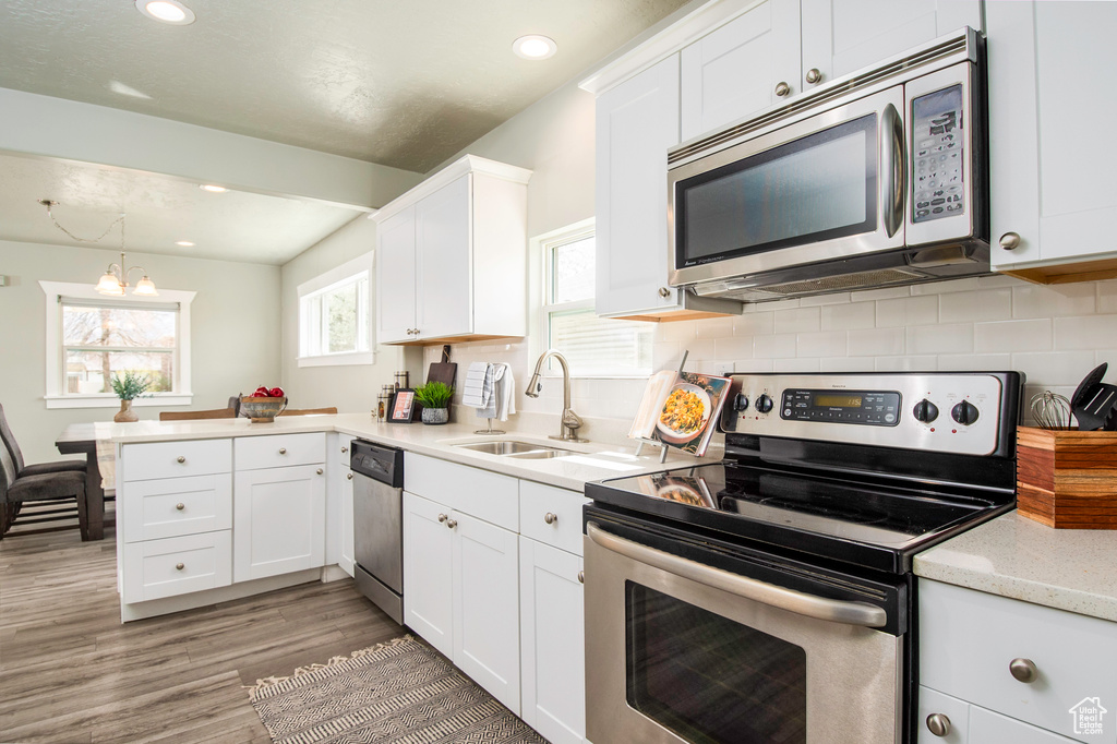 Kitchen with stainless steel appliances, sink, decorative backsplash, light wood-type flooring, and white cabinetry