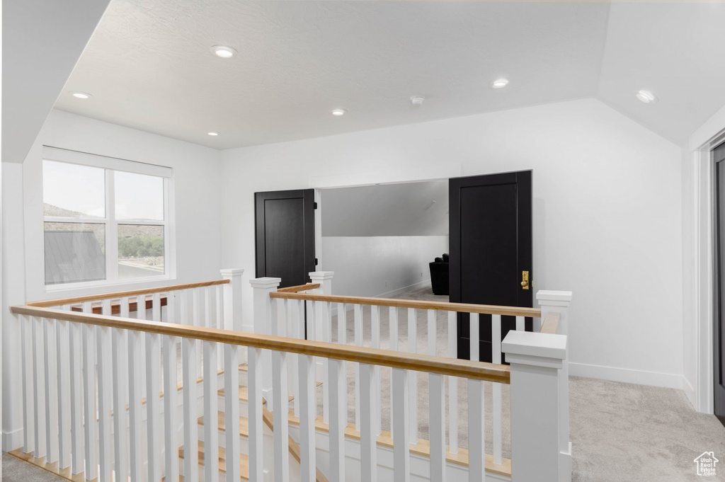 Hallway with lofted ceiling and light colored carpet