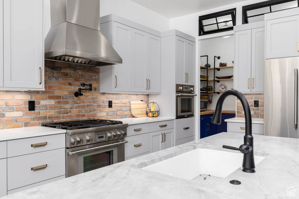 Kitchen featuring sink, light stone counters, high end appliances, and wall chimney exhaust hood