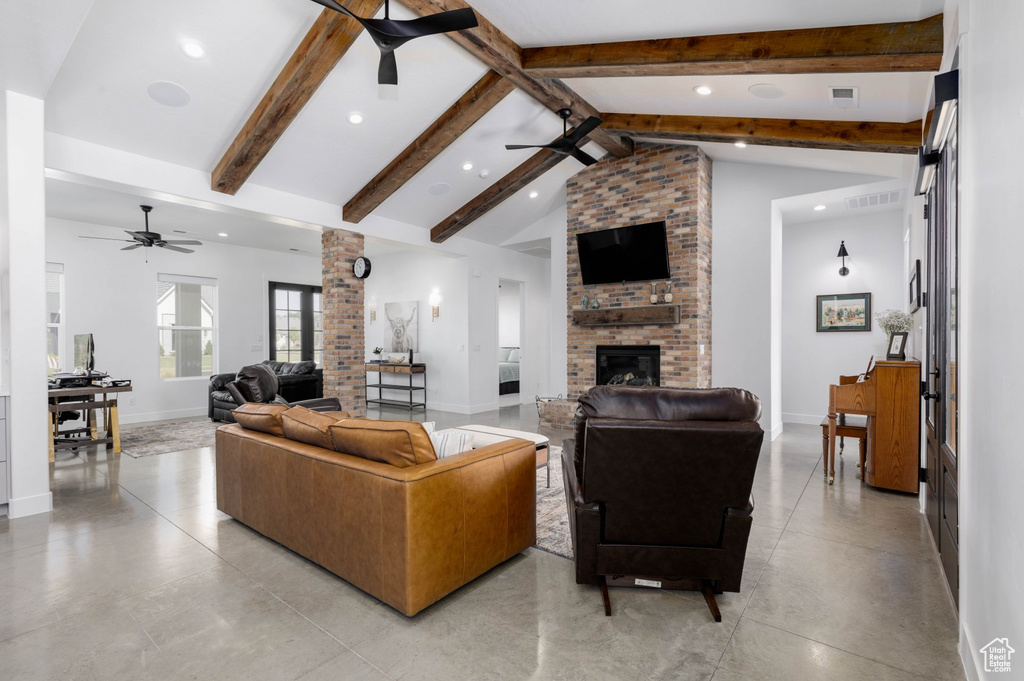 Living room featuring lofted ceiling with beams, ceiling fan, a brick fireplace, and light tile patterned floors