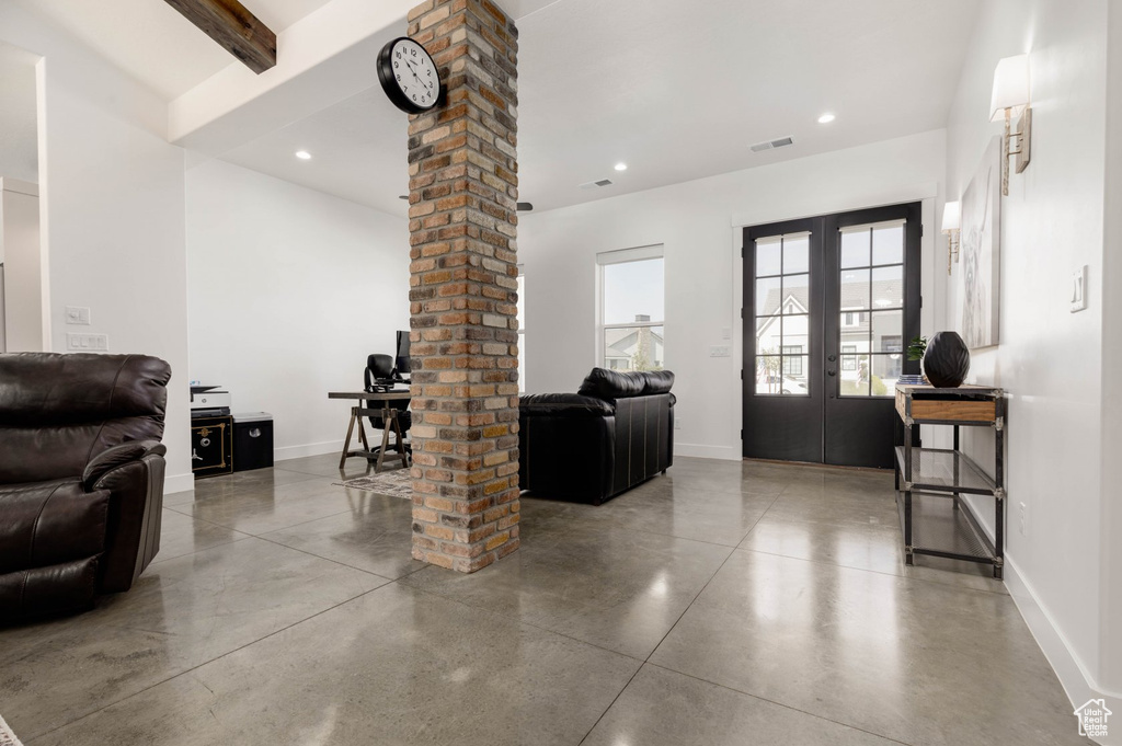 Interior space with concrete flooring, beamed ceiling, brick wall, french doors, and ornate columns