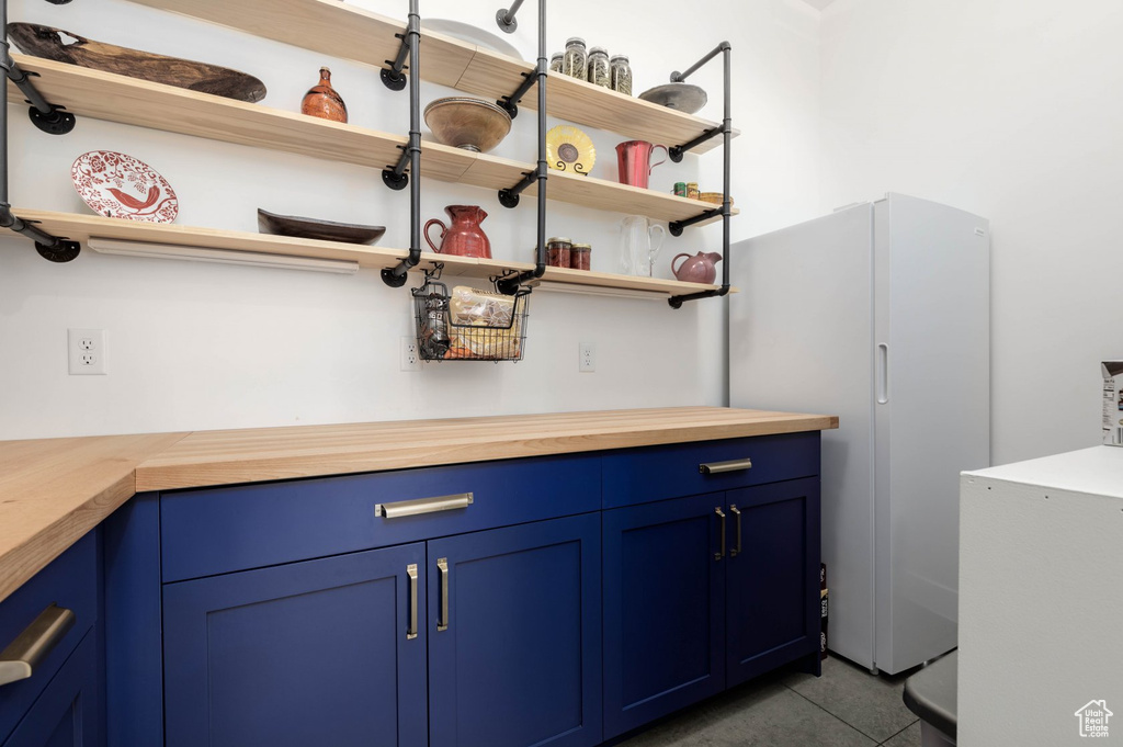 Bar with dark tile patterned floors, white refrigerator, and blue cabinetry