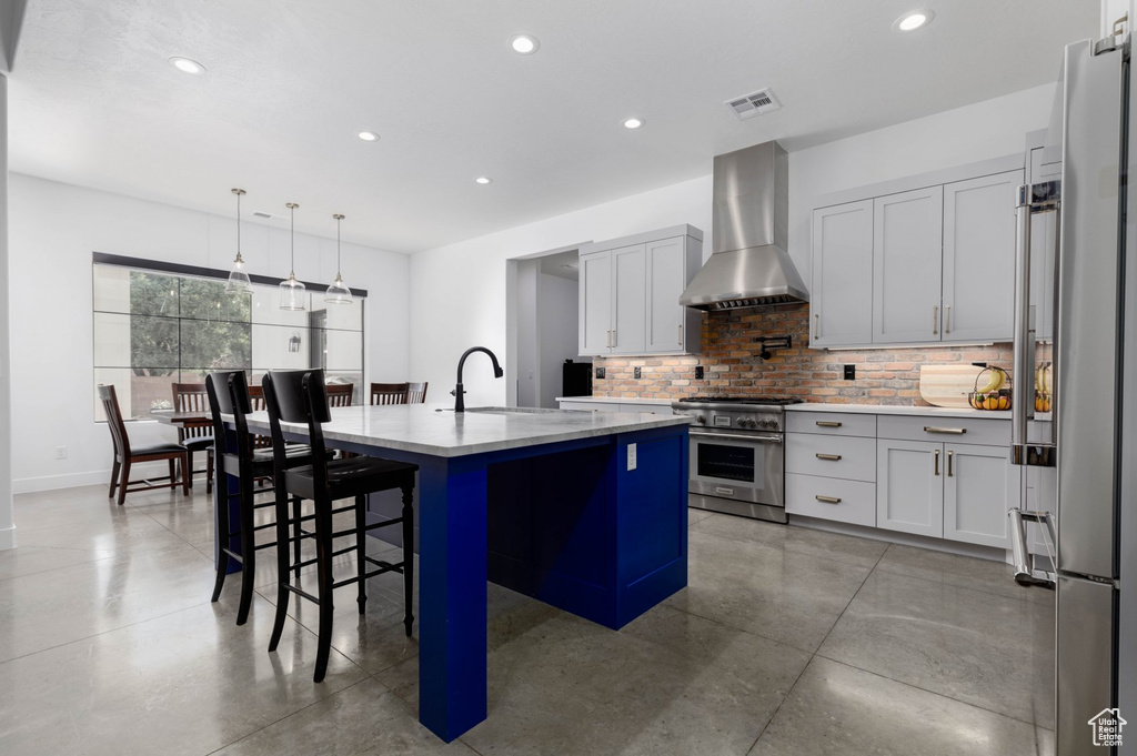 Kitchen featuring tasteful backsplash, wall chimney range hood, an island with sink, sink, and stainless steel stove