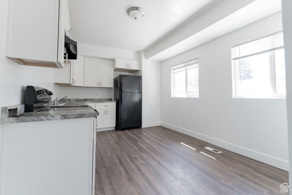 Kitchen with hardwood / wood-style floors, sink, white cabinets, and black refrigerator