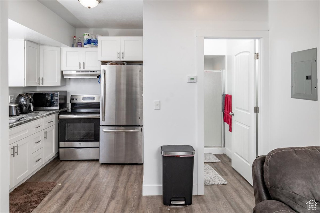 Kitchen with appliances with stainless steel finishes, white cabinetry, electric panel, and hardwood / wood-style flooring