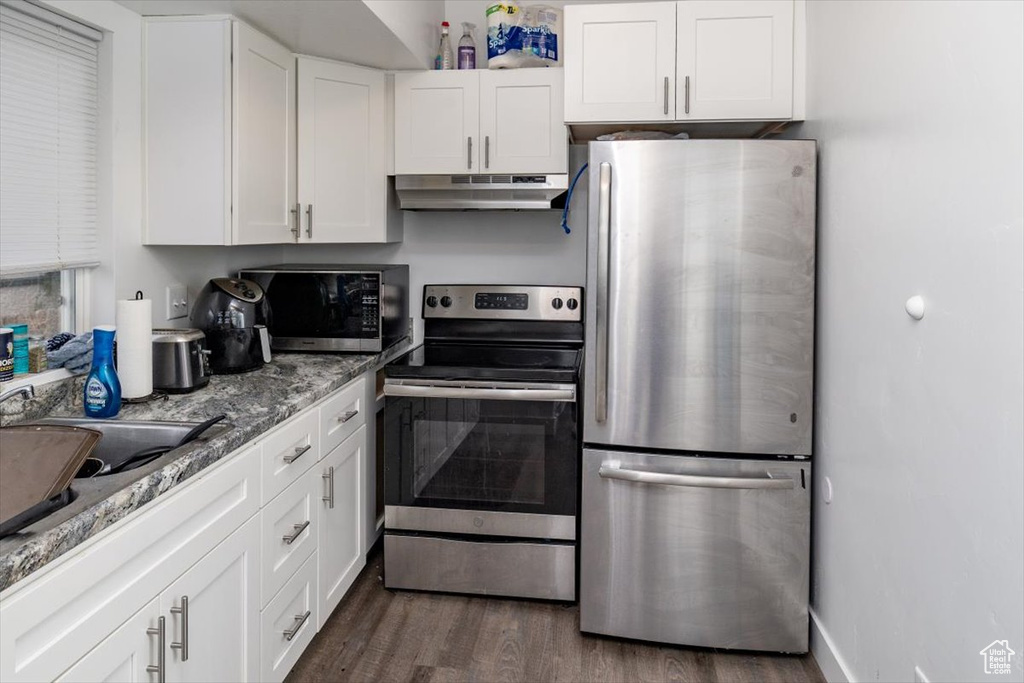 Kitchen with white cabinetry, stainless steel appliances, light stone countertops, and dark hardwood / wood-style flooring