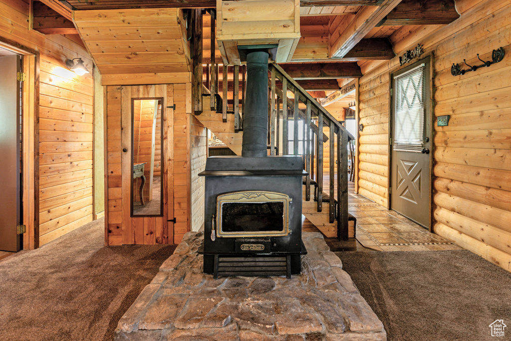 Unfurnished living room featuring beam ceiling, a wood stove, carpet flooring, log walls, and wooden ceiling