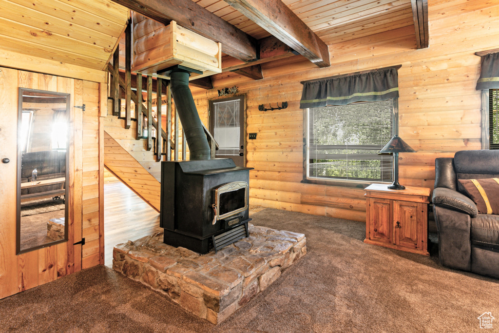 Carpeted living room with wood ceiling, beamed ceiling, rustic walls, and a wood stove