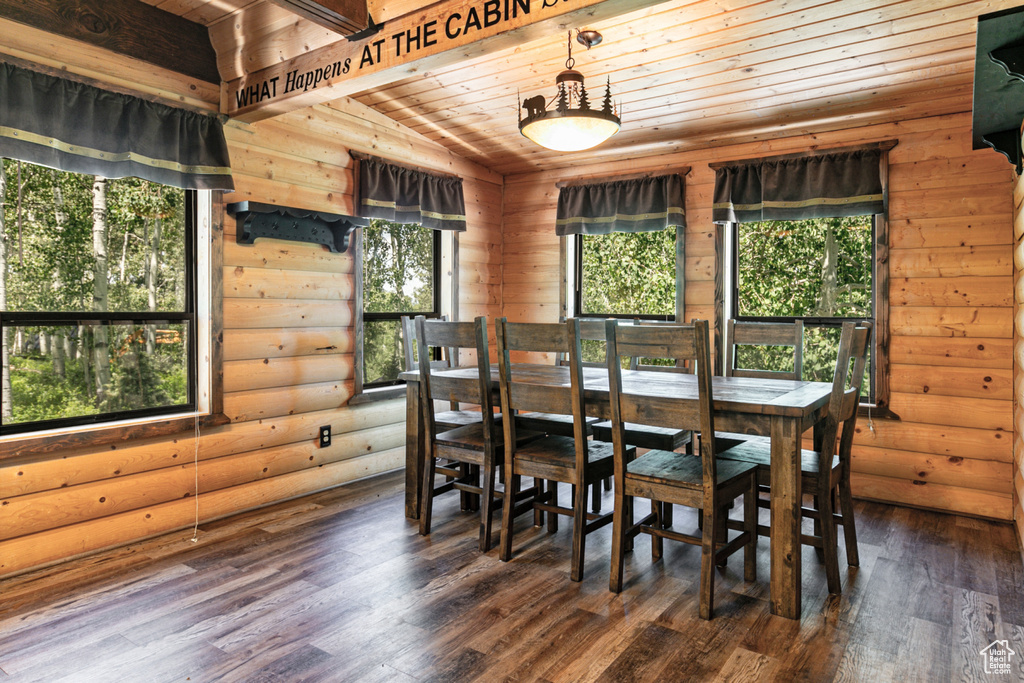 Dining space with dark hardwood / wood-style floors, lofted ceiling, a wealth of natural light, and log walls