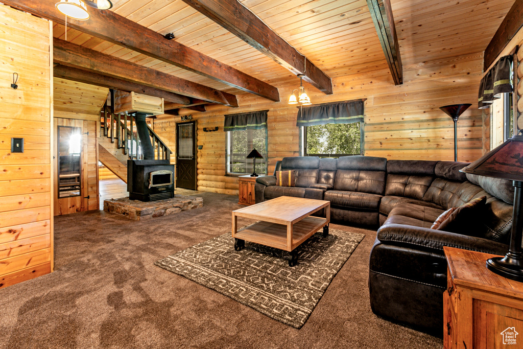 Living room with beam ceiling, a wood stove, wood walls, and carpet floors