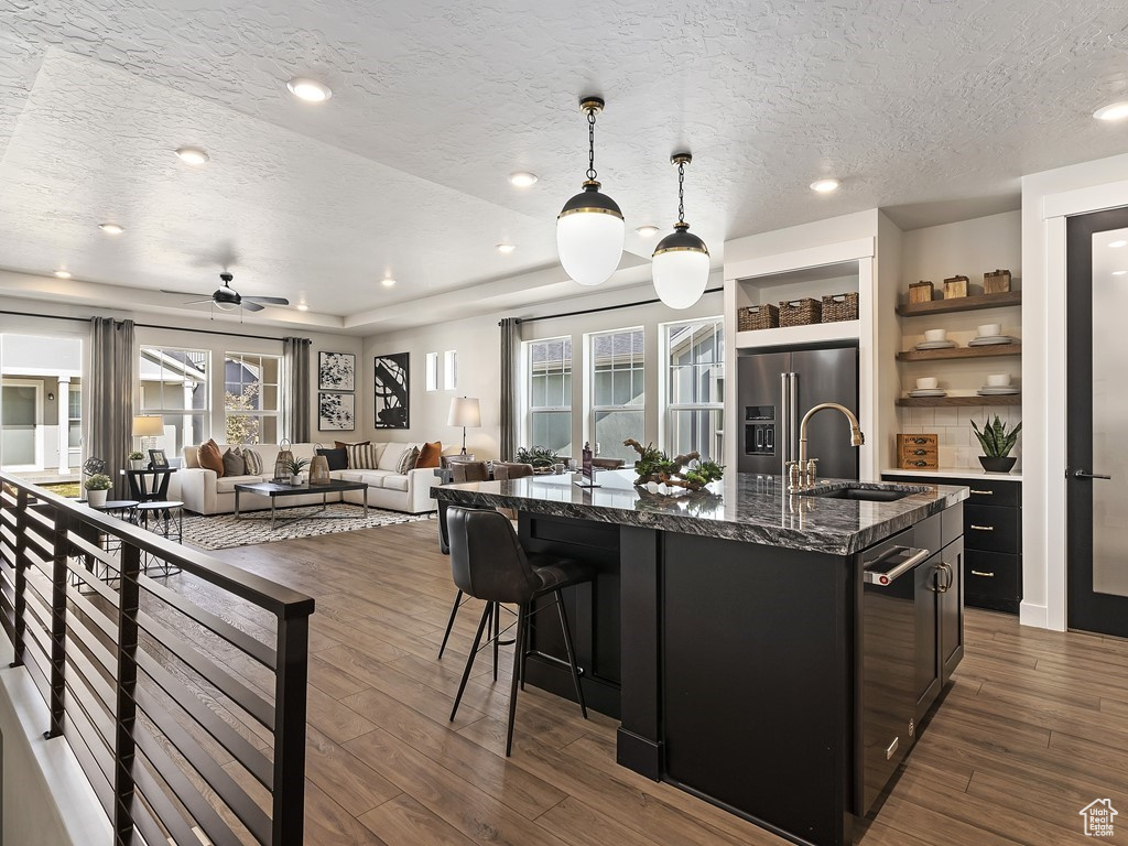 Kitchen featuring dark wood-type flooring, a kitchen island with sink, high end fridge, pendant lighting, and sink