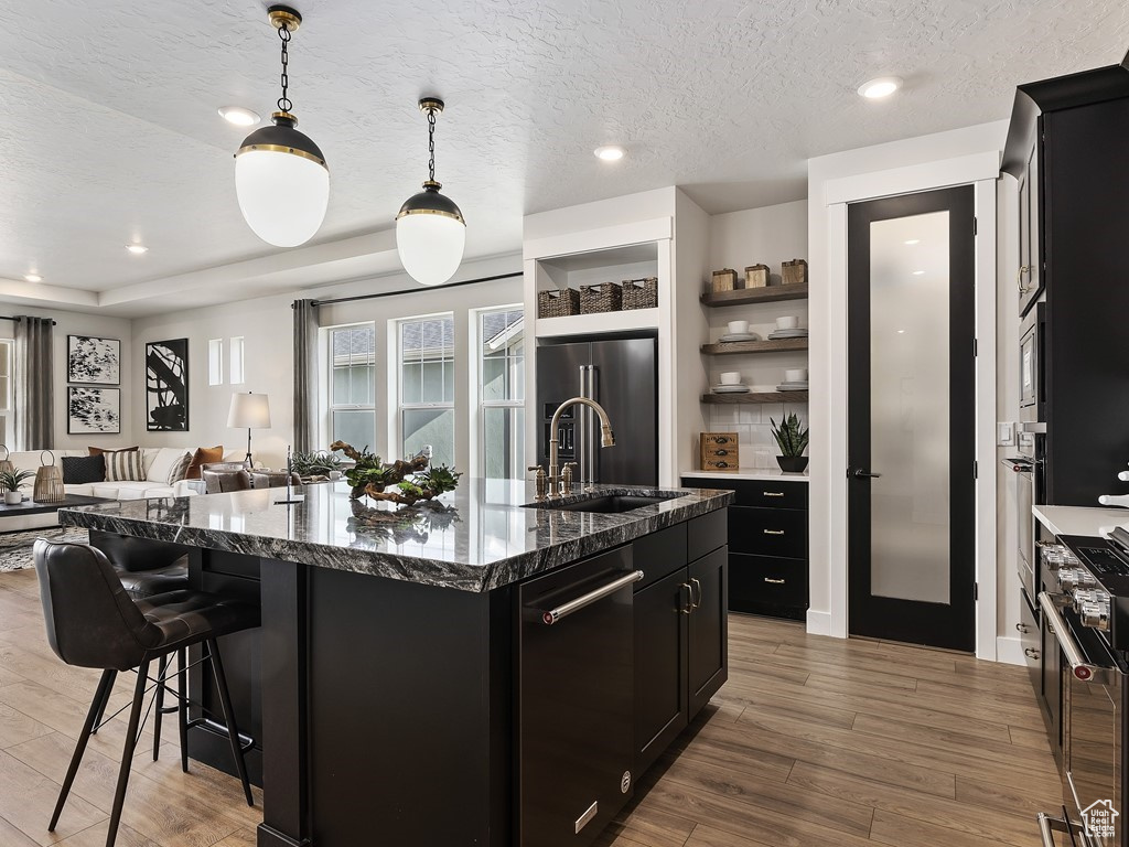 Kitchen with sink, decorative light fixtures, hardwood / wood-style flooring, and a kitchen island with sink