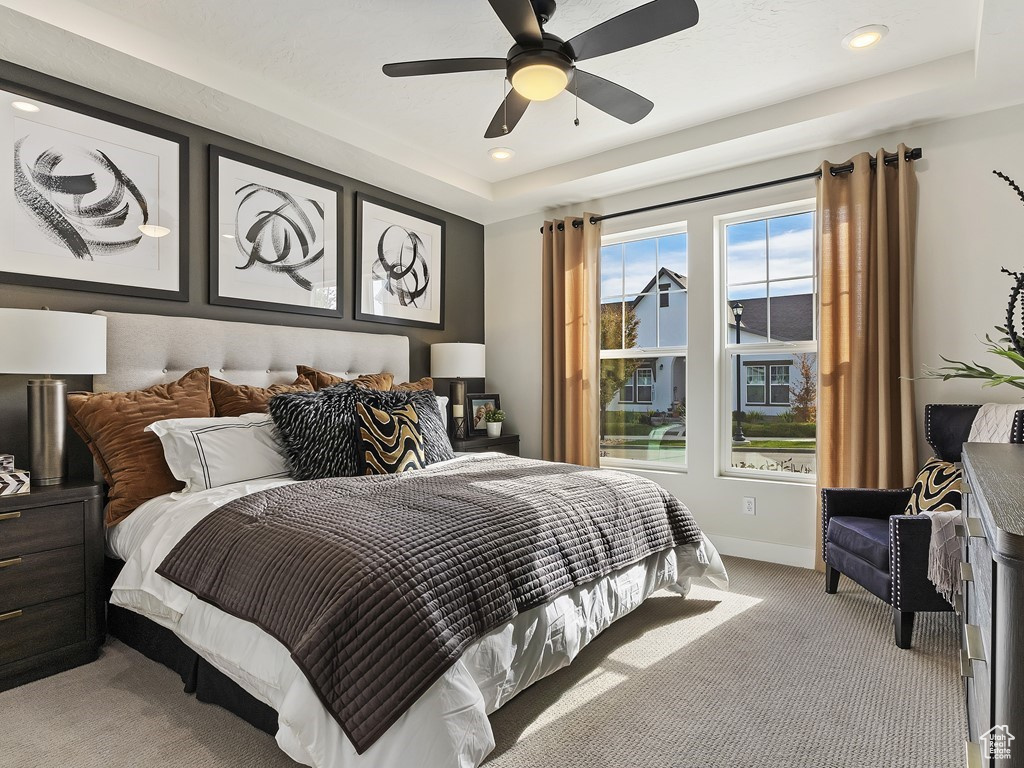 Carpeted bedroom featuring a raised ceiling and ceiling fan