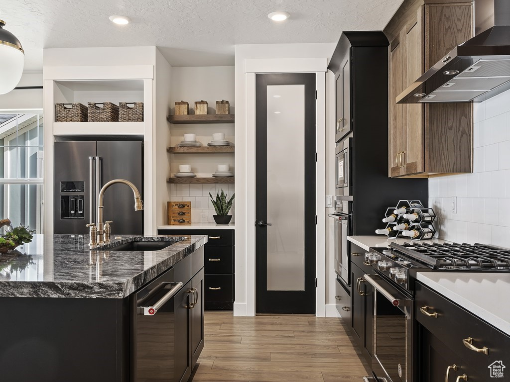 Kitchen featuring sink, high quality appliances, decorative backsplash, and wall chimney range hood