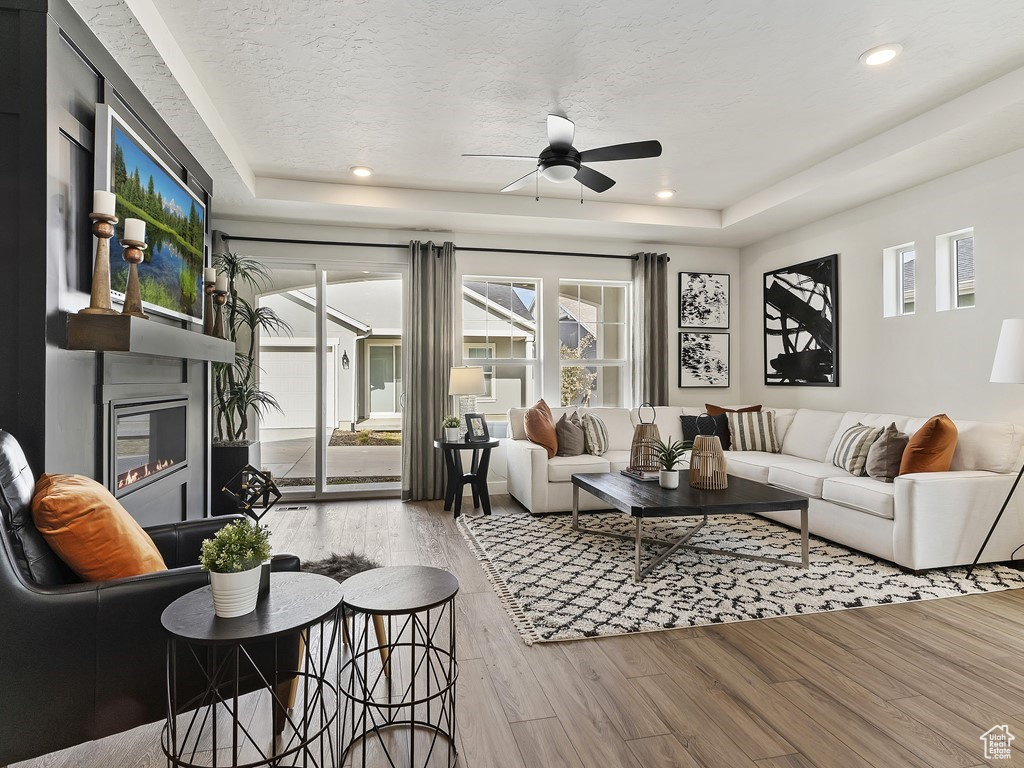 Living room featuring ceiling fan, a tray ceiling, a textured ceiling, and light hardwood / wood-style flooring