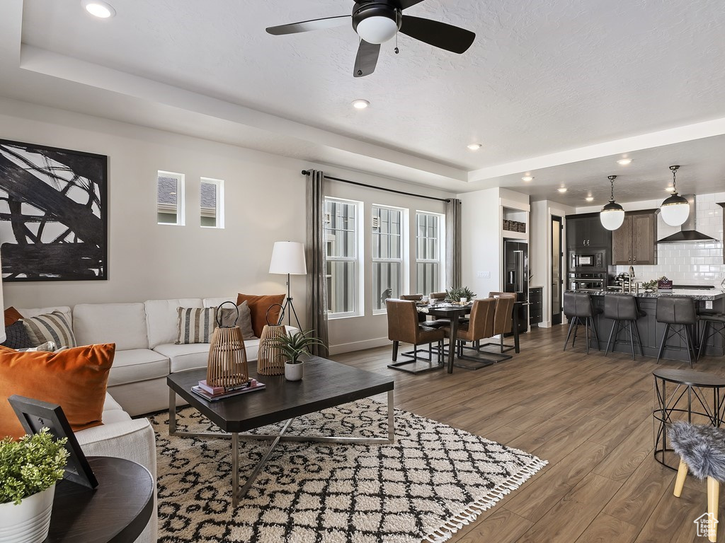 Living room featuring ceiling fan, hardwood / wood-style flooring, a raised ceiling, and a wealth of natural light