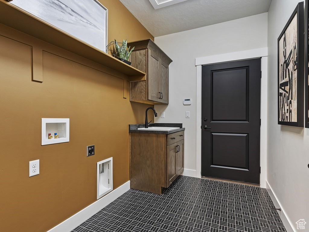 Laundry area featuring dark tile patterned floors, hookup for a washing machine, cabinets, electric dryer hookup, and sink