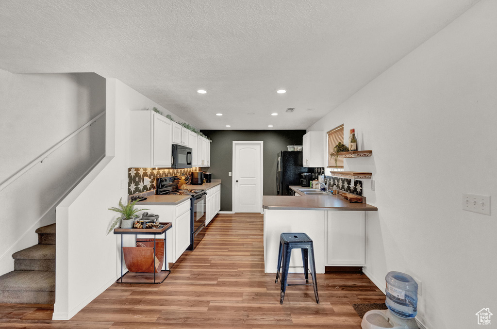 Kitchen with kitchen peninsula, white cabinets, light hardwood / wood-style floors, black appliances, and a kitchen breakfast bar