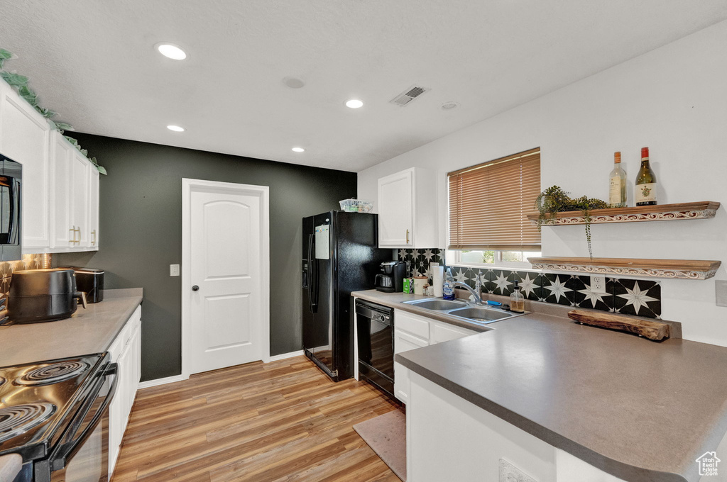 Kitchen with black appliances, white cabinets, sink, light hardwood / wood-style floors, and backsplash