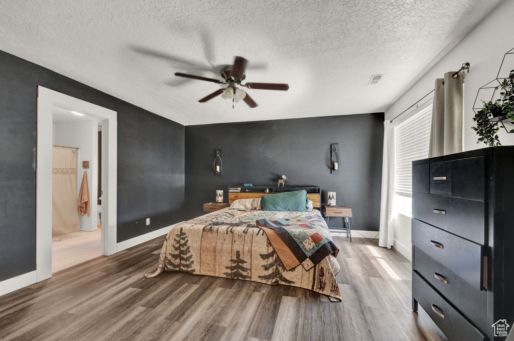 Bedroom with hardwood / wood-style flooring, a textured ceiling, ensuite bathroom, and ceiling fan