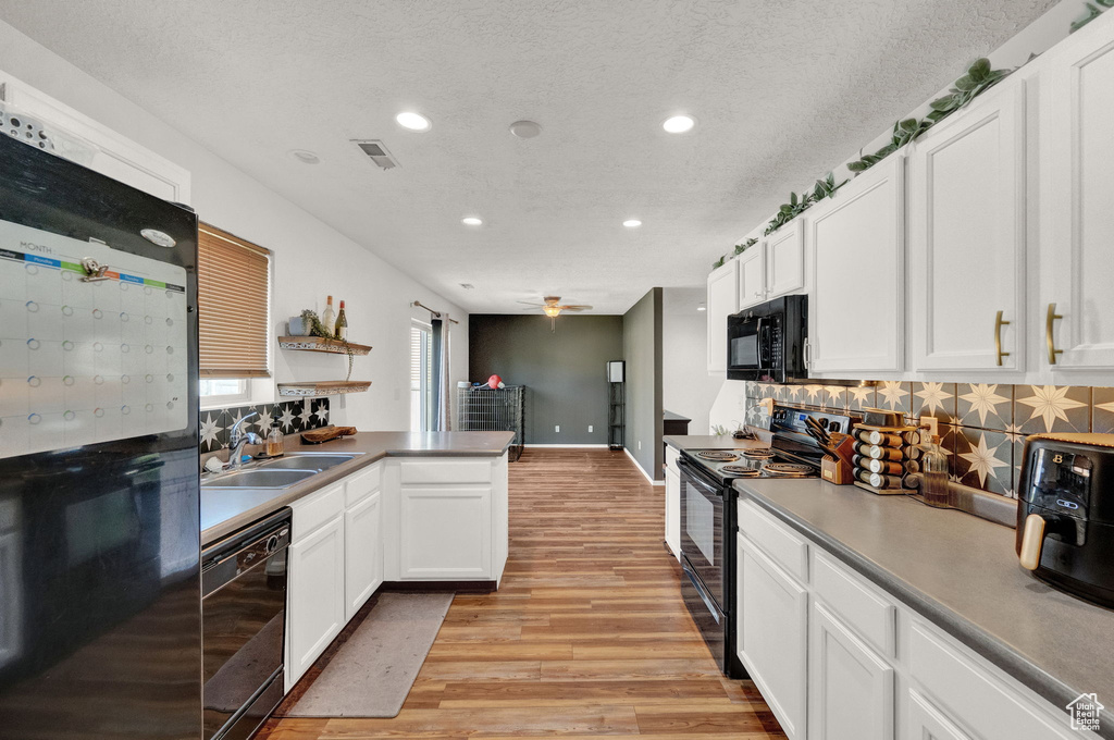 Kitchen featuring light wood-type flooring, white cabinets, black appliances, decorative backsplash, and sink