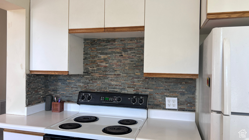 Kitchen featuring white fridge, white cabinets, range, and decorative backsplash