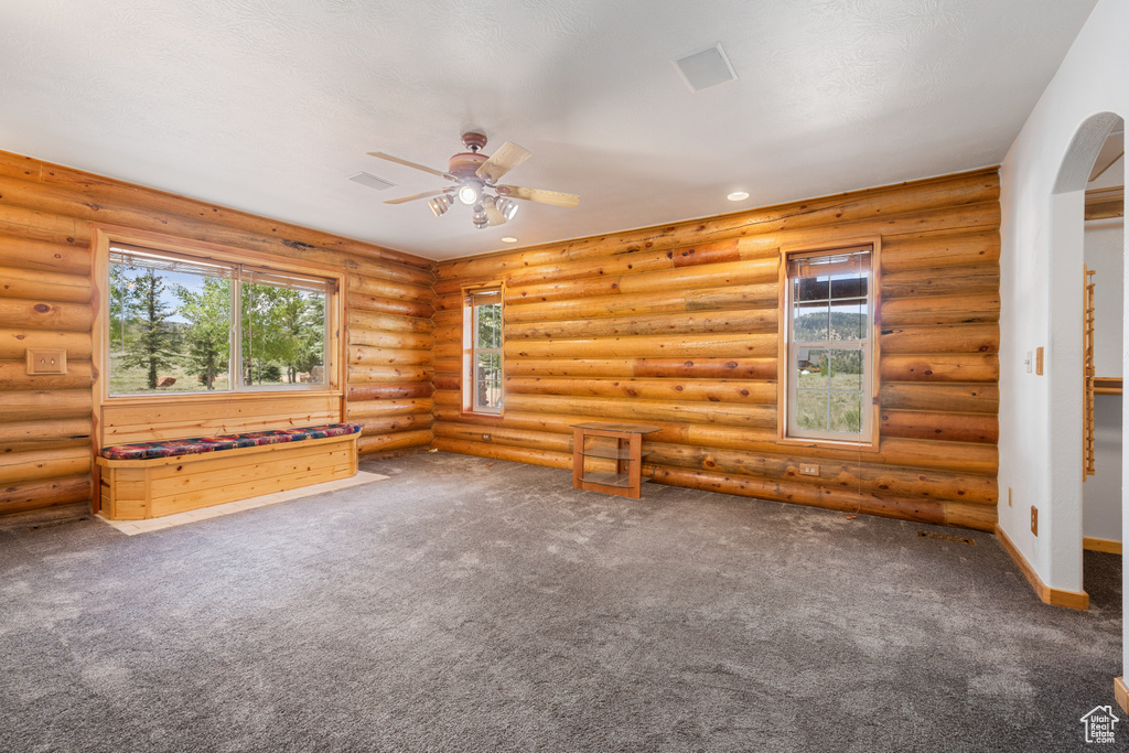 Unfurnished living room with carpet flooring, ceiling fan, and log walls