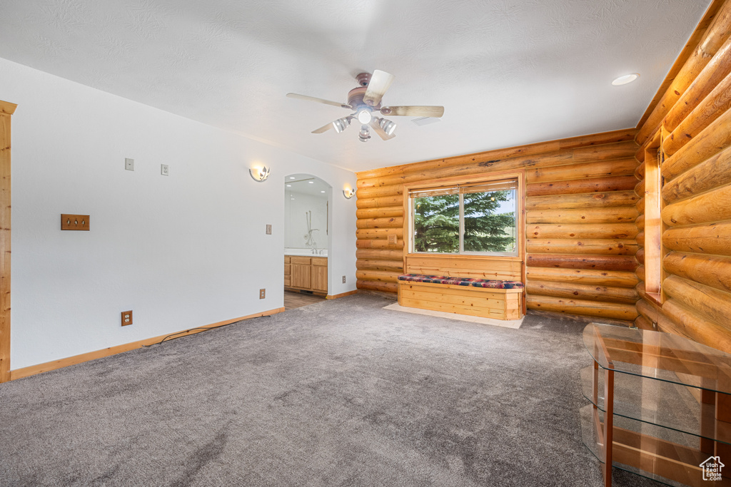 Unfurnished living room with log walls, carpet, and ceiling fan