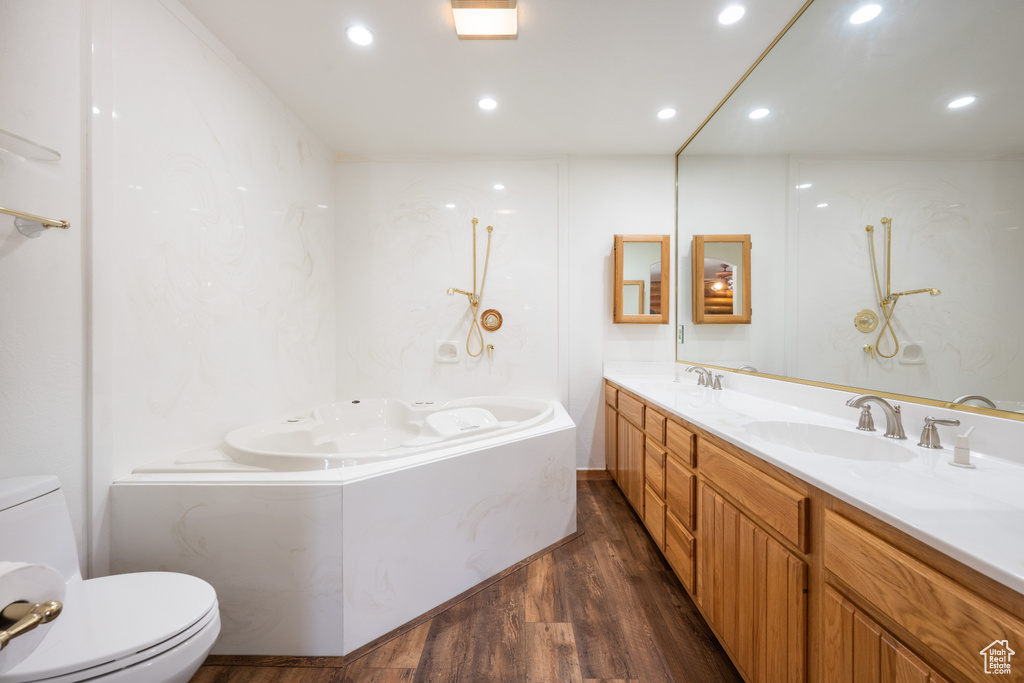 Bathroom with double vanity, wood-type flooring, toilet, and a relaxing tiled tub