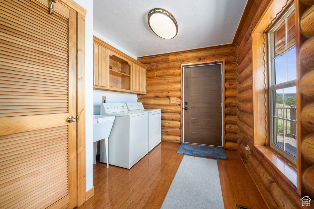 Laundry area with cabinets, hardwood / wood-style floors, independent washer and dryer, and log walls