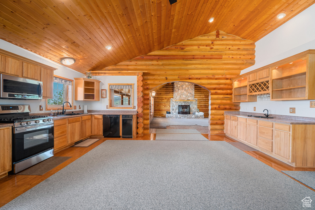 Kitchen with a fireplace, rustic walls, sink, light hardwood / wood-style floors, and appliances with stainless steel finishes