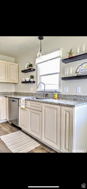 Kitchen featuring light stone countertops, stainless steel dishwasher, decorative light fixtures, sink, and wood-type flooring