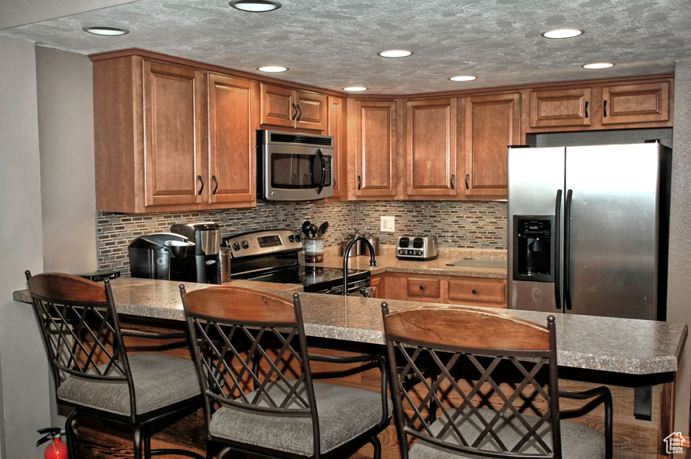 Kitchen featuring decorative backsplash, appliances with stainless steel finishes, a textured ceiling, and a breakfast bar