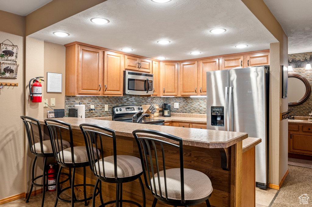 Kitchen with a kitchen breakfast bar, kitchen peninsula, appliances with stainless steel finishes, and a textured ceiling