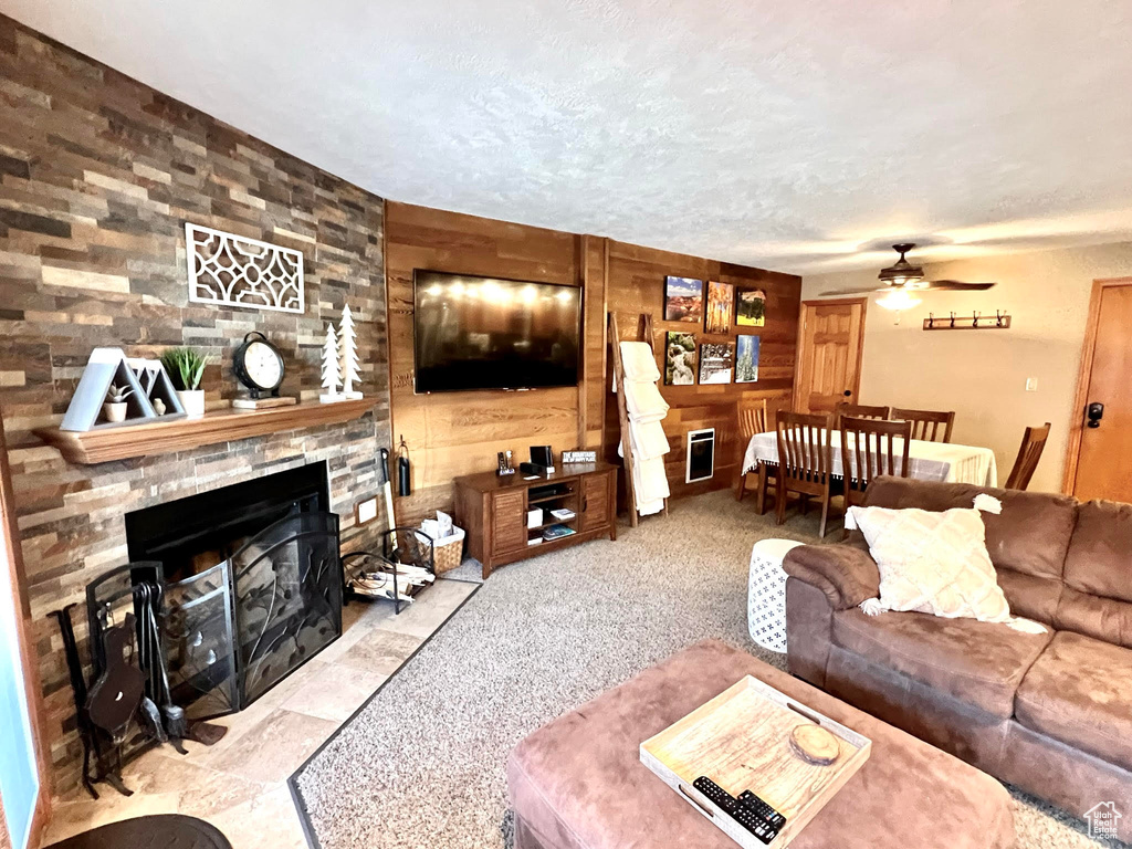 Living room featuring a stone fireplace, ceiling fan, carpet, and wooden walls