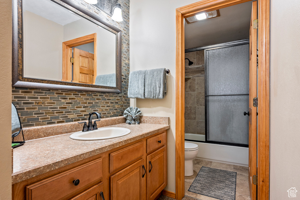 Full bathroom with decorative backsplash, vanity, enclosed tub / shower combo, toilet, and tile patterned floors