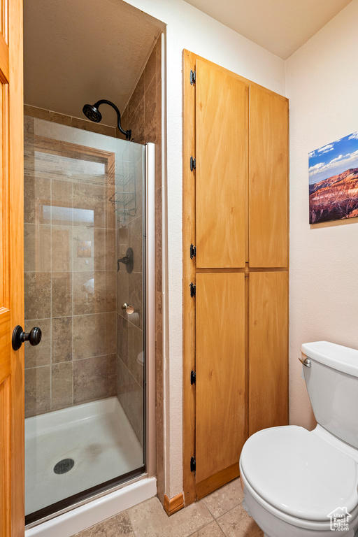 Bathroom featuring toilet, a shower with door, and tile patterned floors