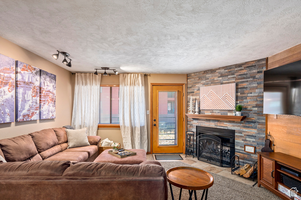 Carpeted living room featuring a textured ceiling, rail lighting, a stone fireplace, and wood walls