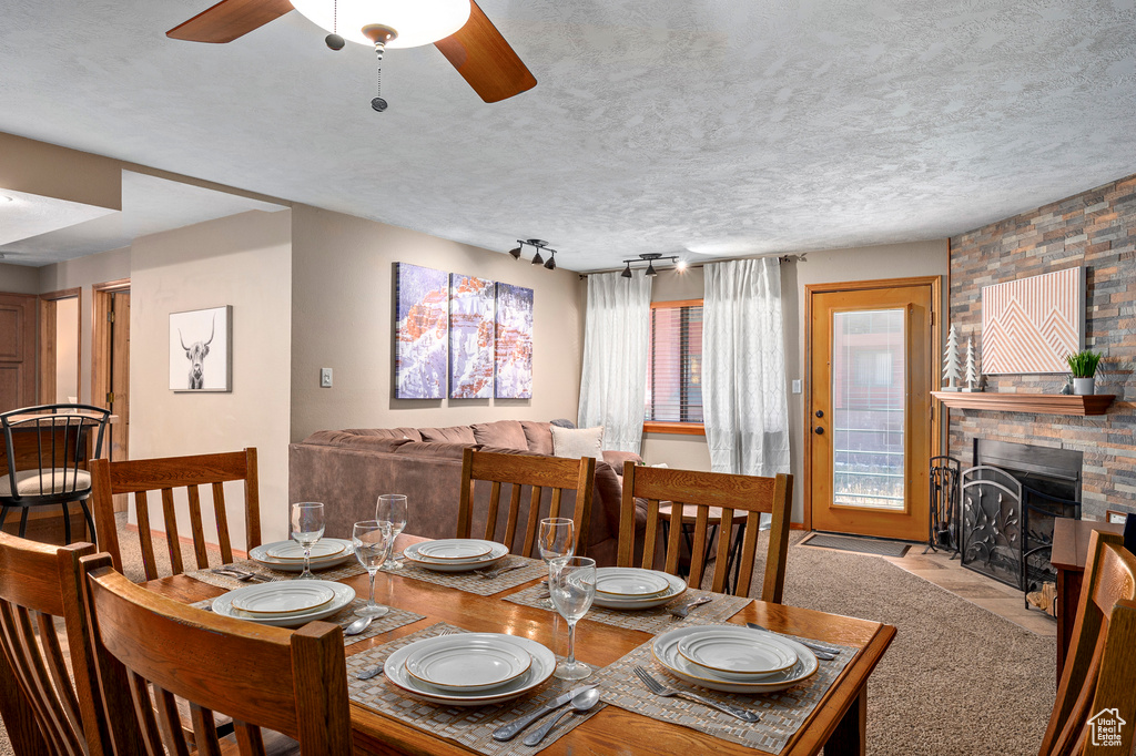 Dining space with a textured ceiling, light colored carpet, rail lighting, a brick fireplace, and ceiling fan