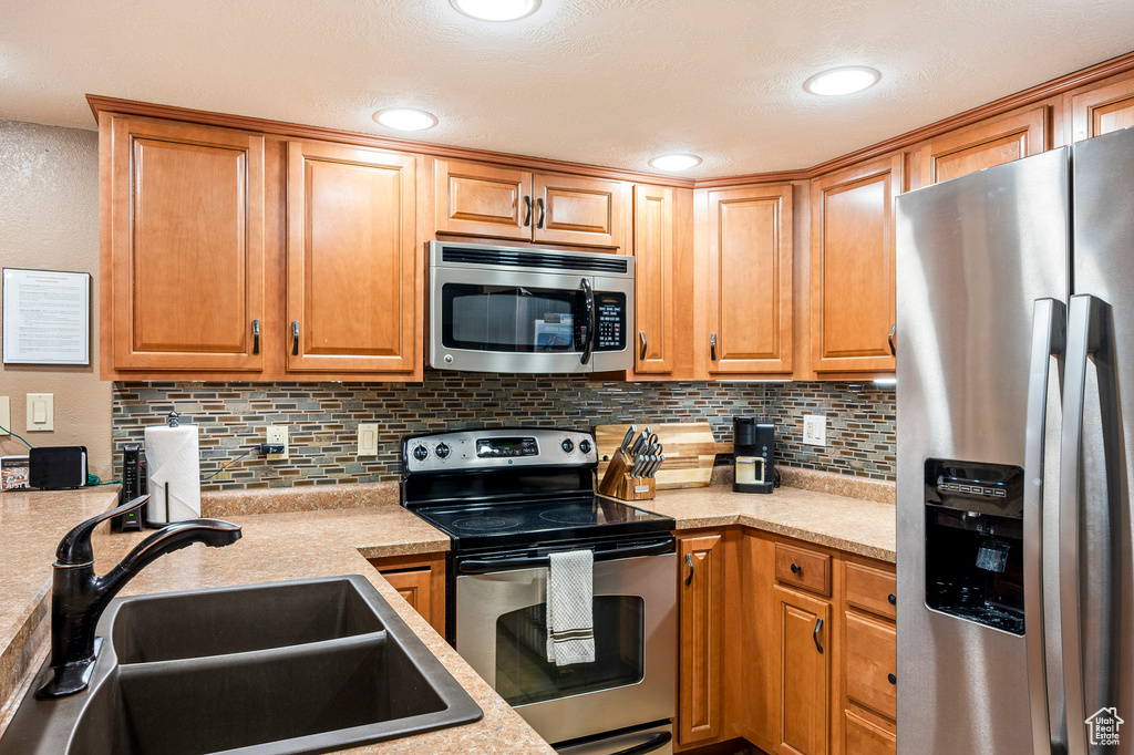 Kitchen featuring appliances with stainless steel finishes, backsplash, a textured ceiling, and sink