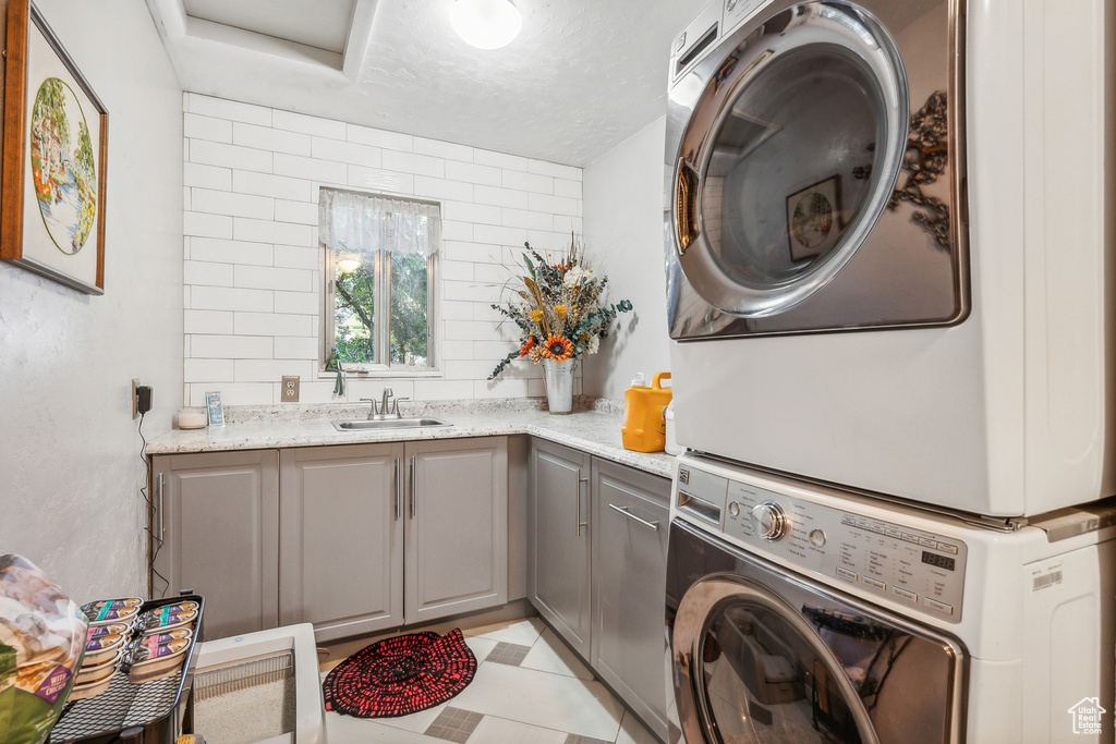 Laundry room featuring cabinets, sink, stacked washer and dryer, and light tile floors