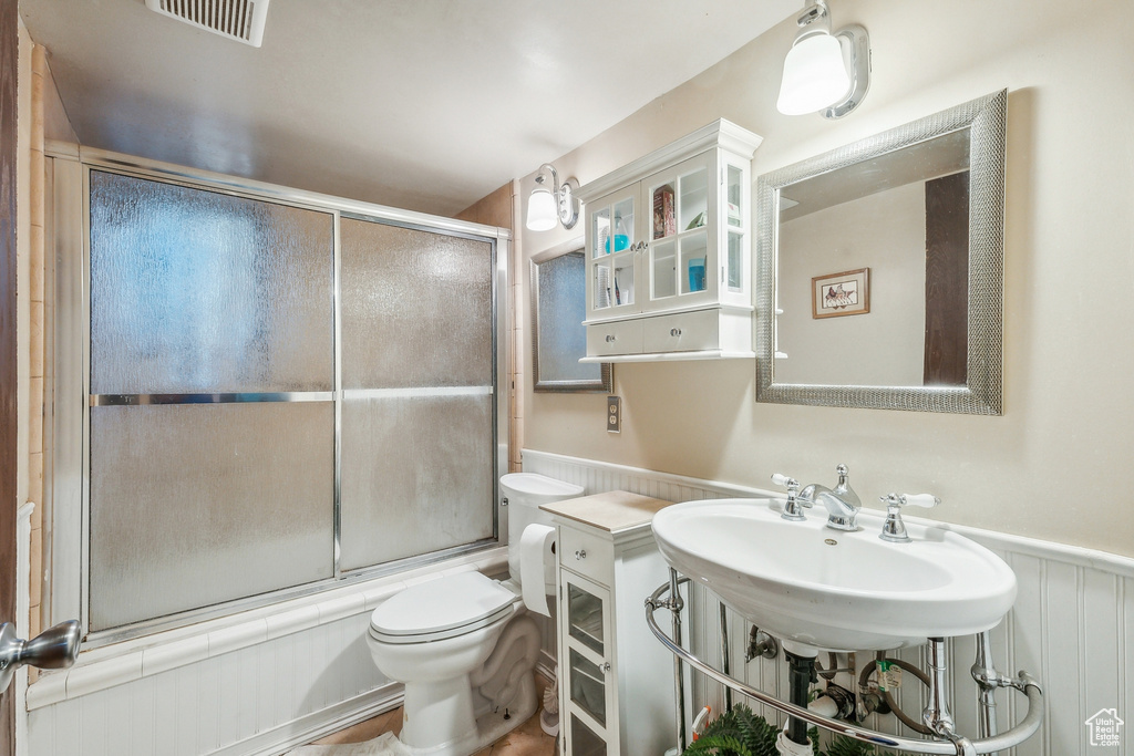 Bathroom featuring bath / shower combo with glass door and toilet