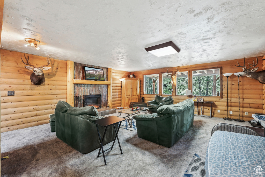 Carpeted living room featuring a fireplace, a textured ceiling, and log walls